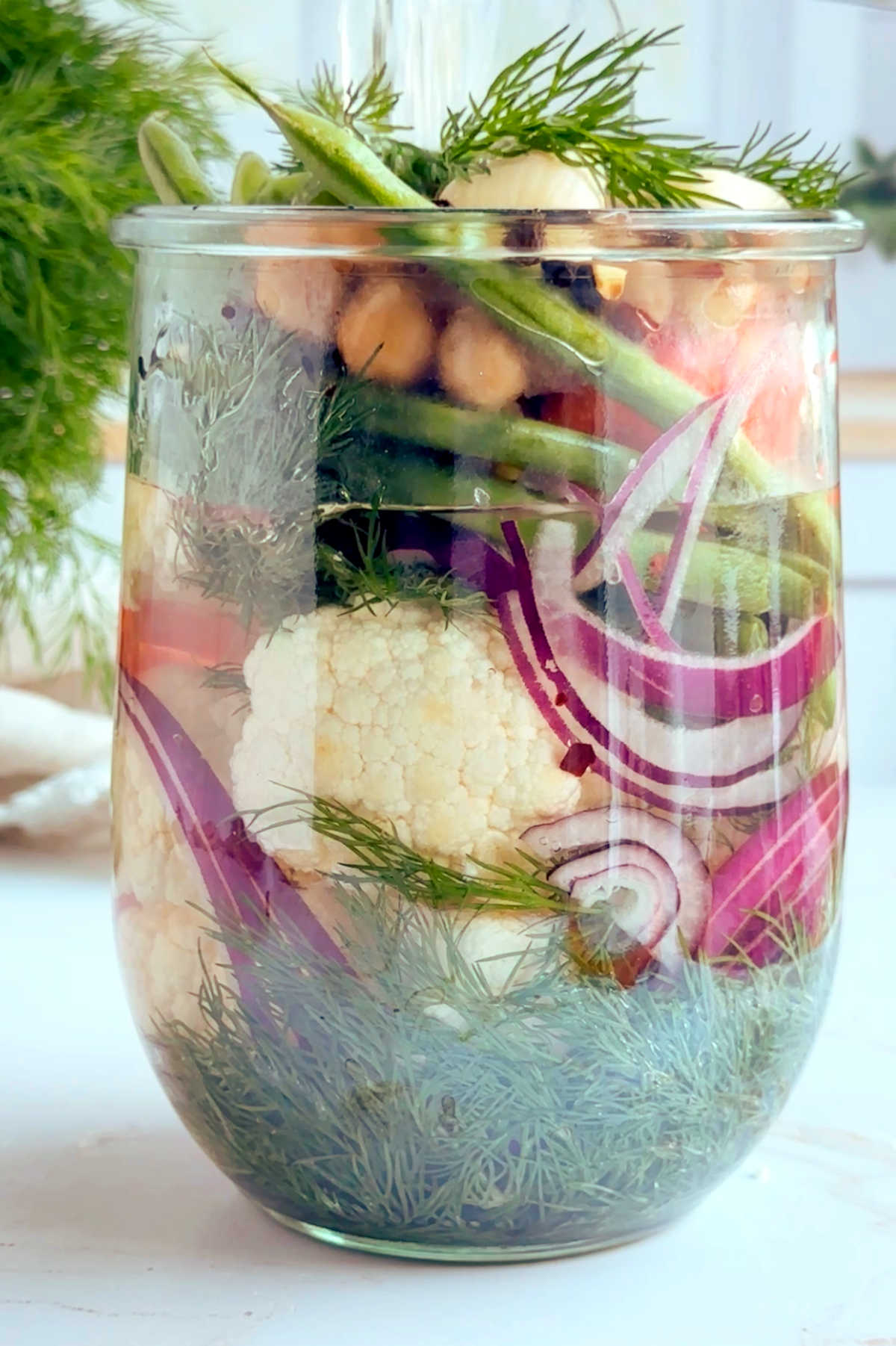 Mixed vegetables in a glass jar with pickling brine being poured over.