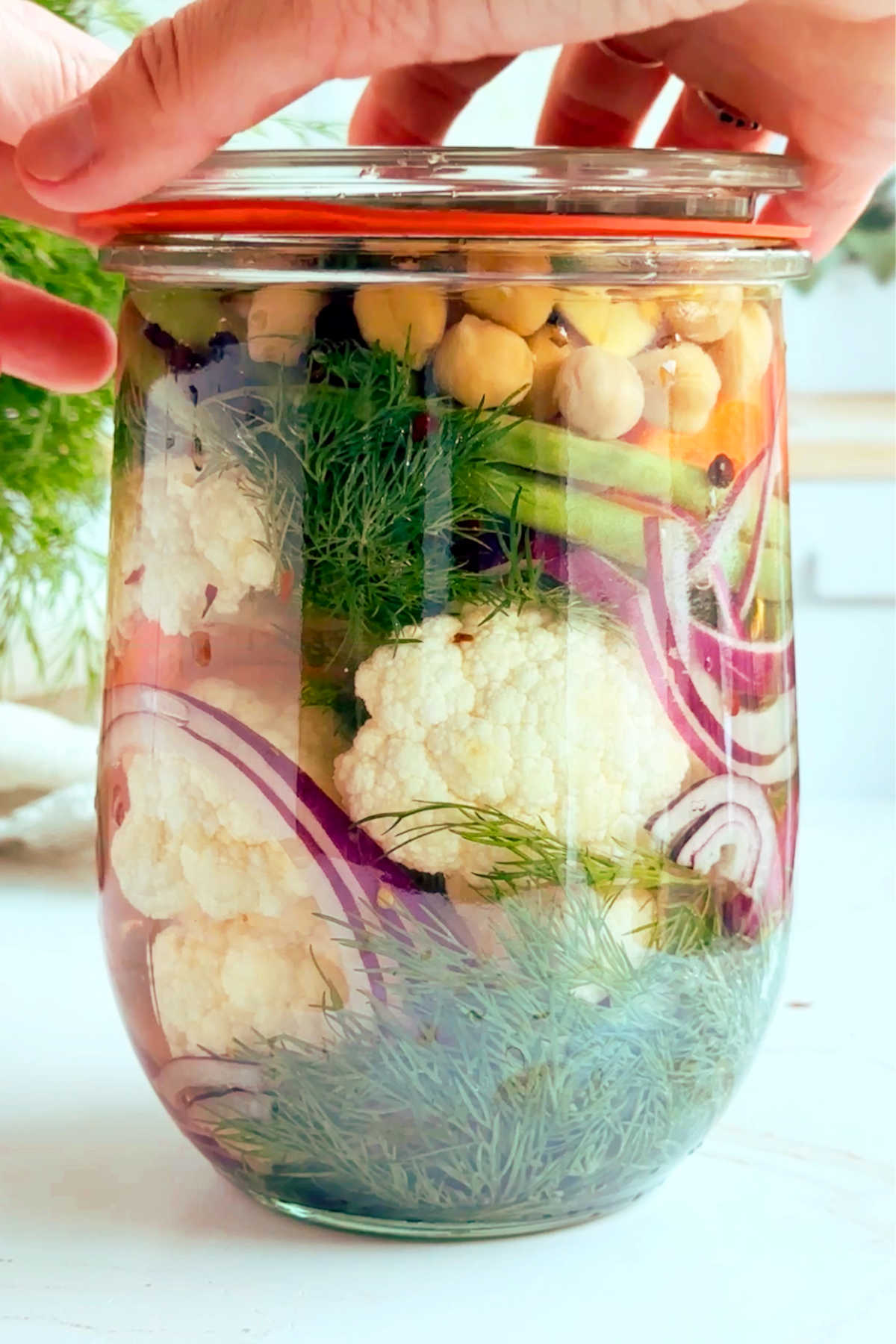 Hands covering the mixed pickles vegetables jar with a lid.