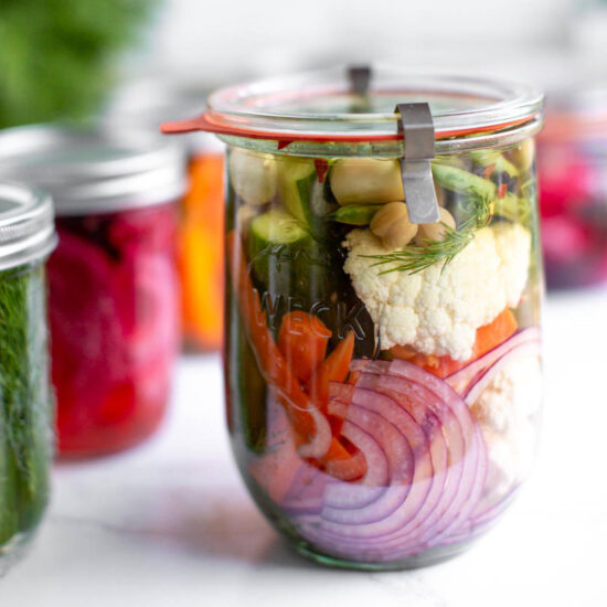 Mixed pickled vegetables in a glass jar filled with pickling brine.