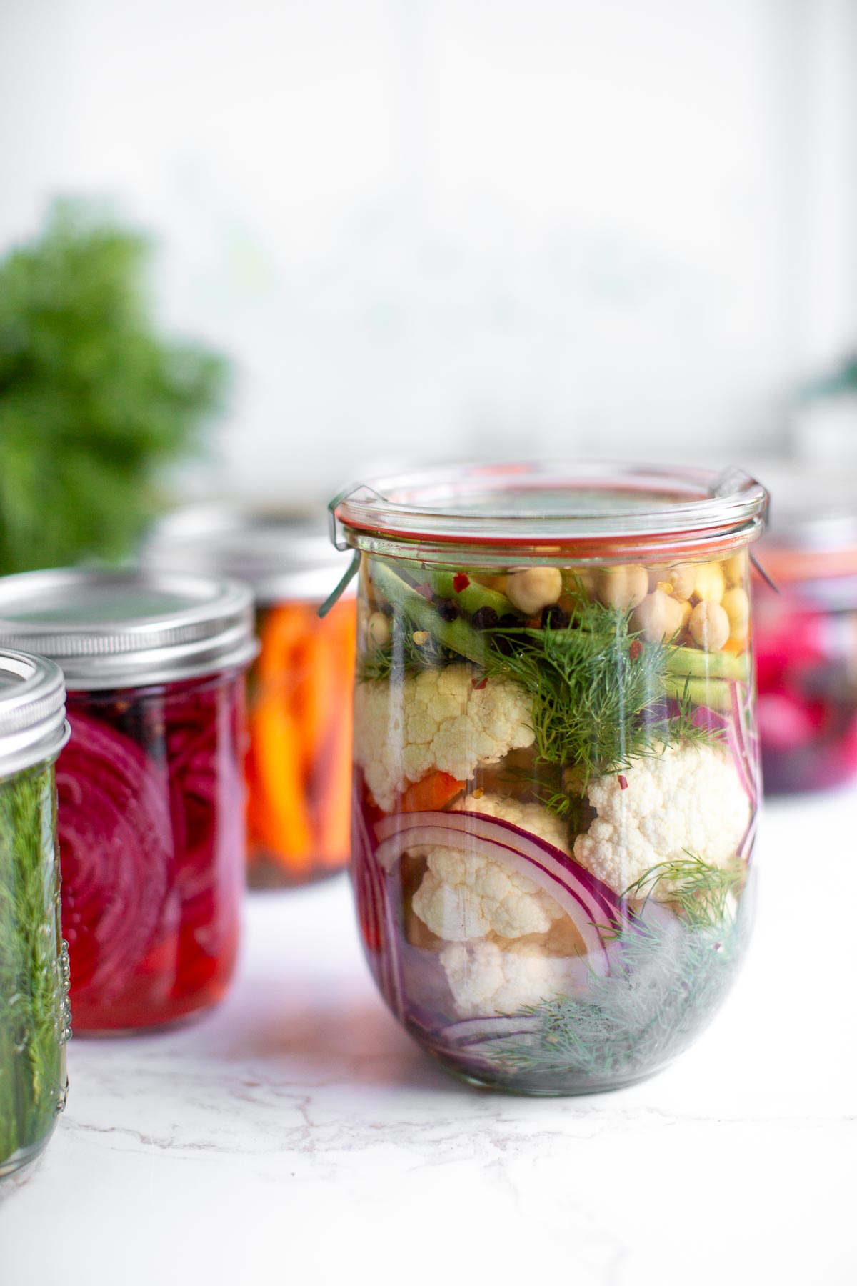 A jar of mixed pickled veggies including red onion, cauliflower, chickpeas, carrots, green beans, and garlic.