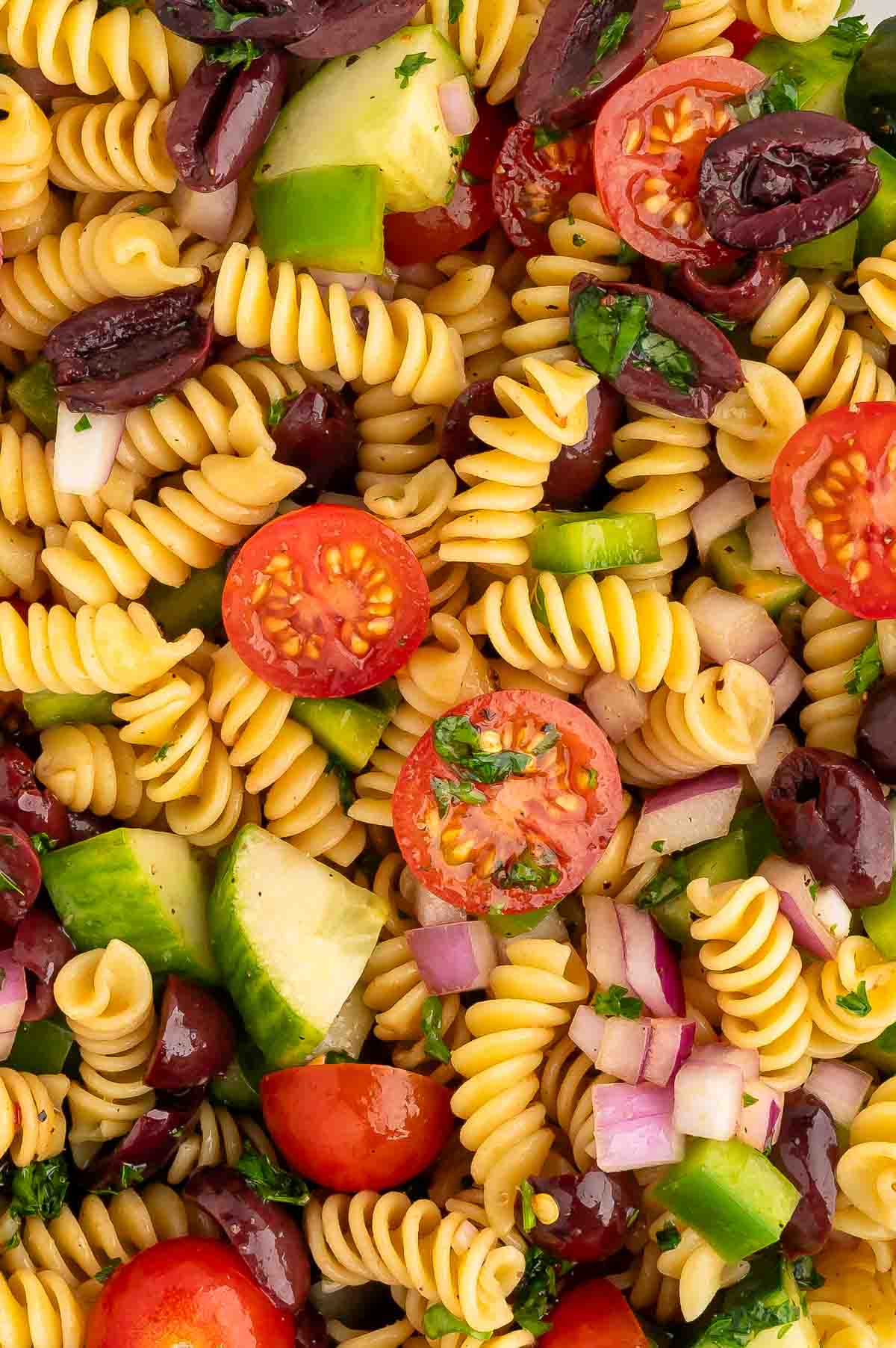 Vegan pasta salad with noodles, cherry tomatoes, olives, cucumber, and bell peppers tossed in dressing.