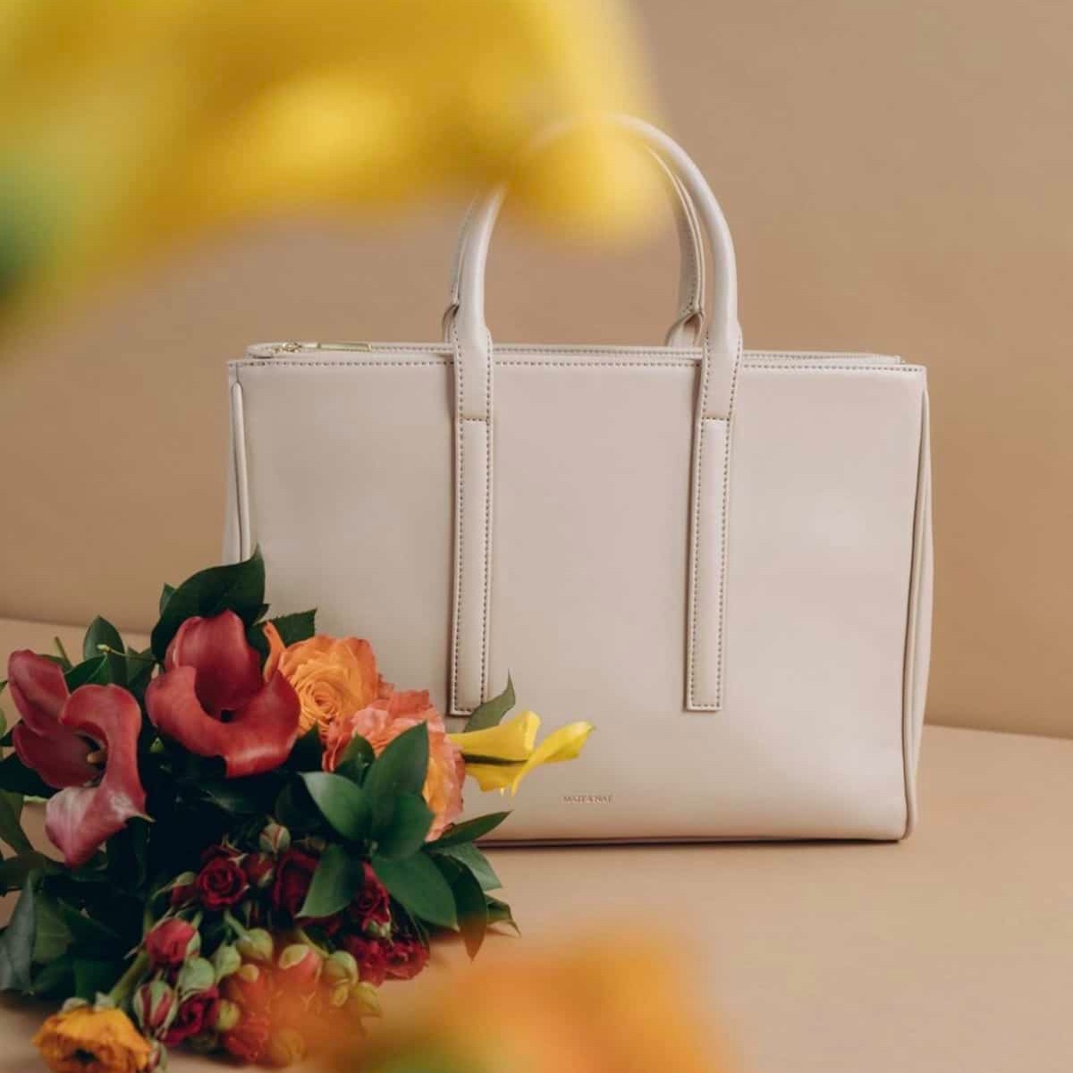 Beautiful white vegan leather handbag purse from on a table with a bouquet of flowers.