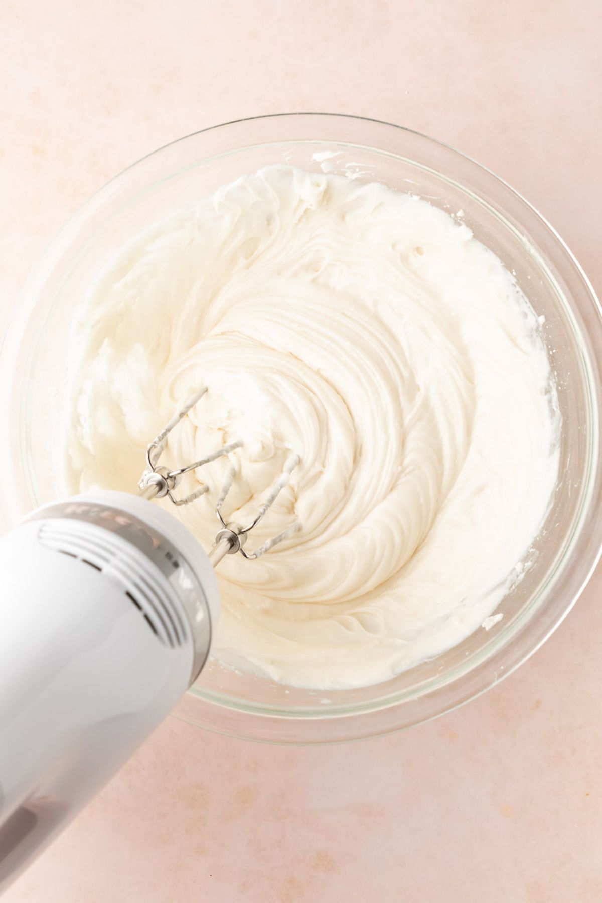 Vegan cream cheese frosting being whipped until light and fluffy in a mixing bowl.