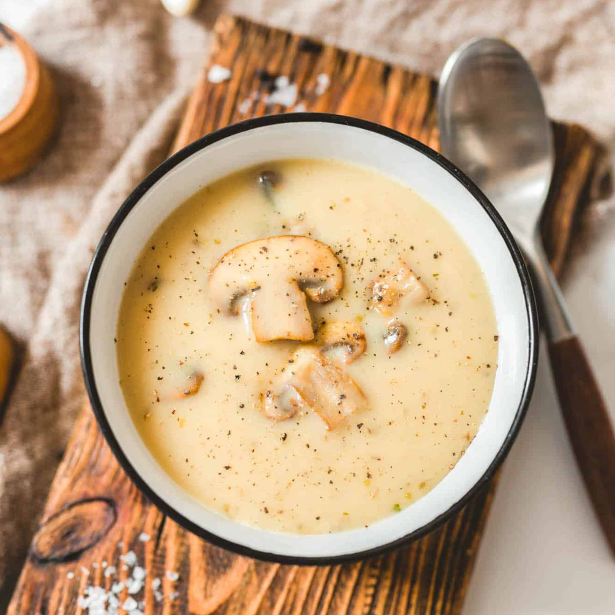 Vegan cream of mushroom soup in a bowl with sliced mushrooms and cracked black pepper on top.