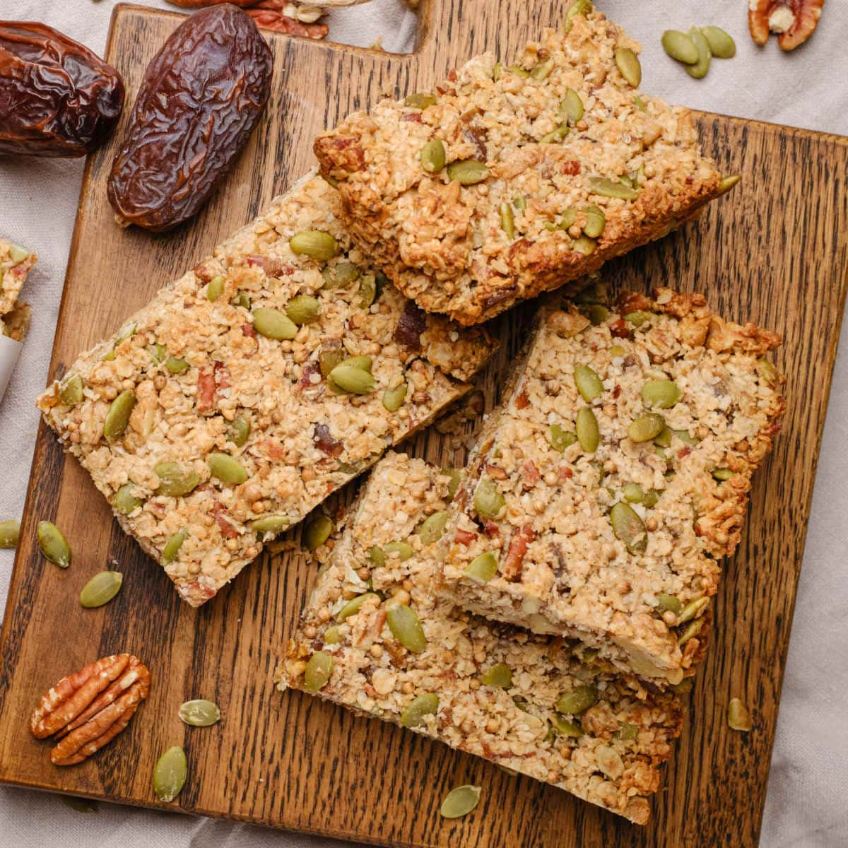 Vegan granola bars on a wooden cutting board surrounded by nuts and seeds.