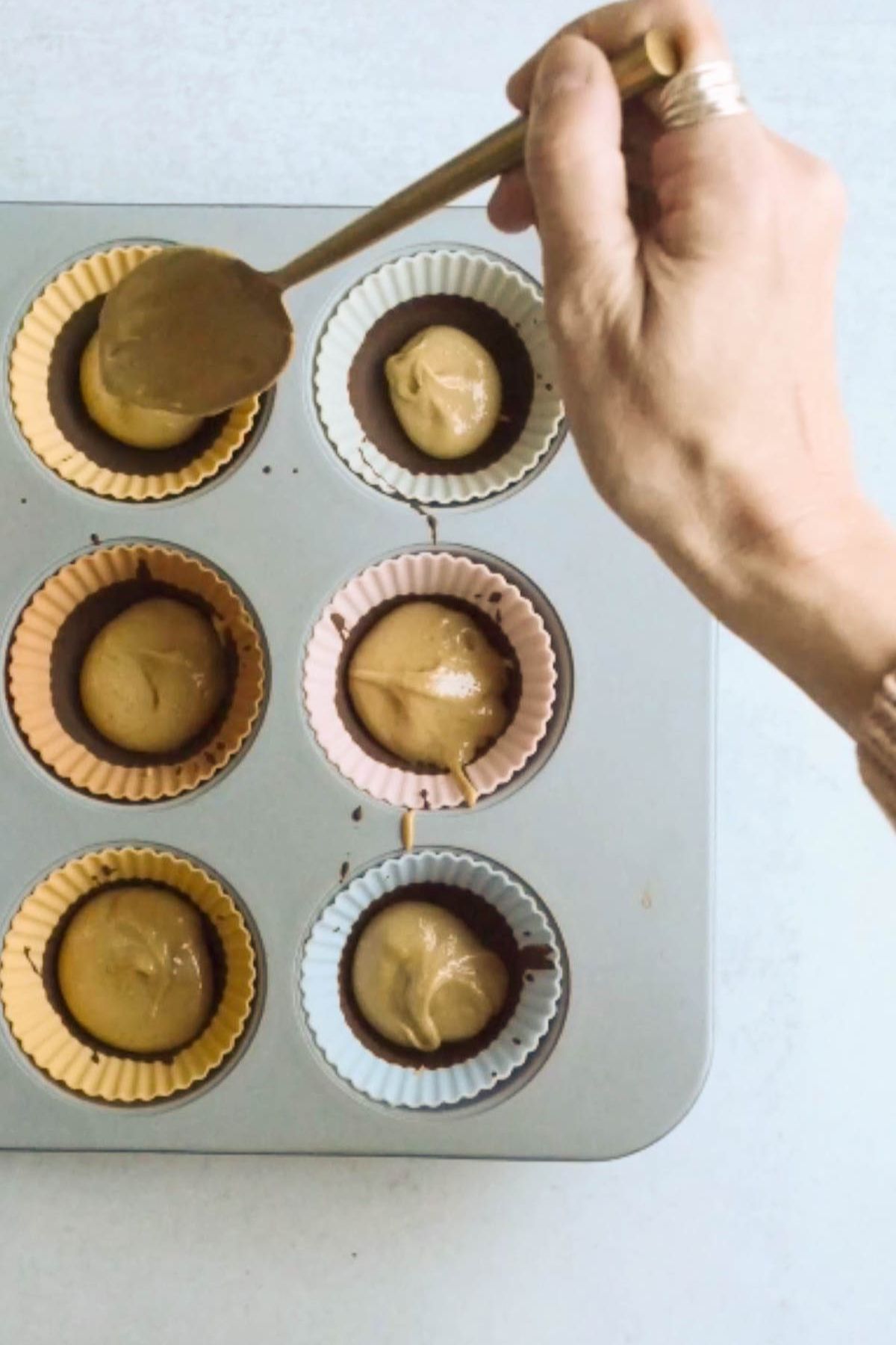 Peanut butter being spooned into a muffin tin.