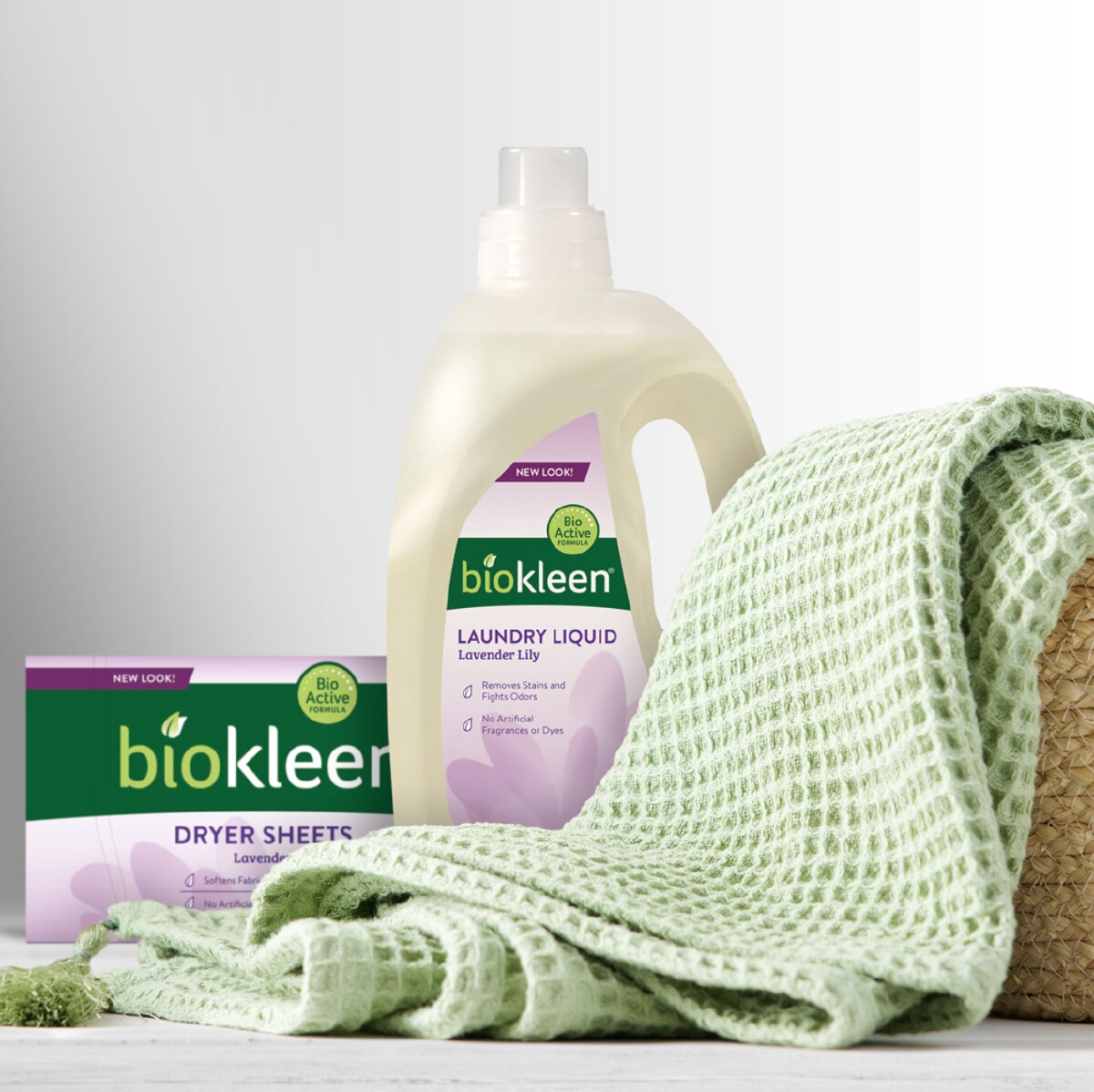 A box of BioKleen dryer sheets and a clear plastic jug of BioKleen laundry detergent next to a light green waffle towel. 