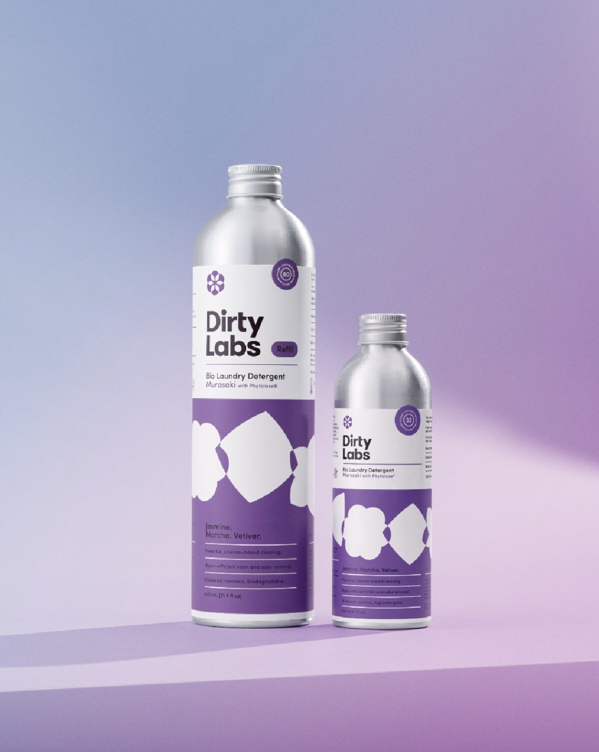 A large and small aluminum bottle of Dirty Labs laundry detergent against a purple background.