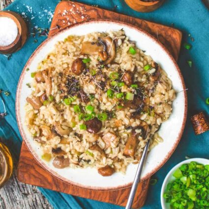 A bowl of vegan mushroom risotto on white plate garnished with green onions and chopped mushrooms.