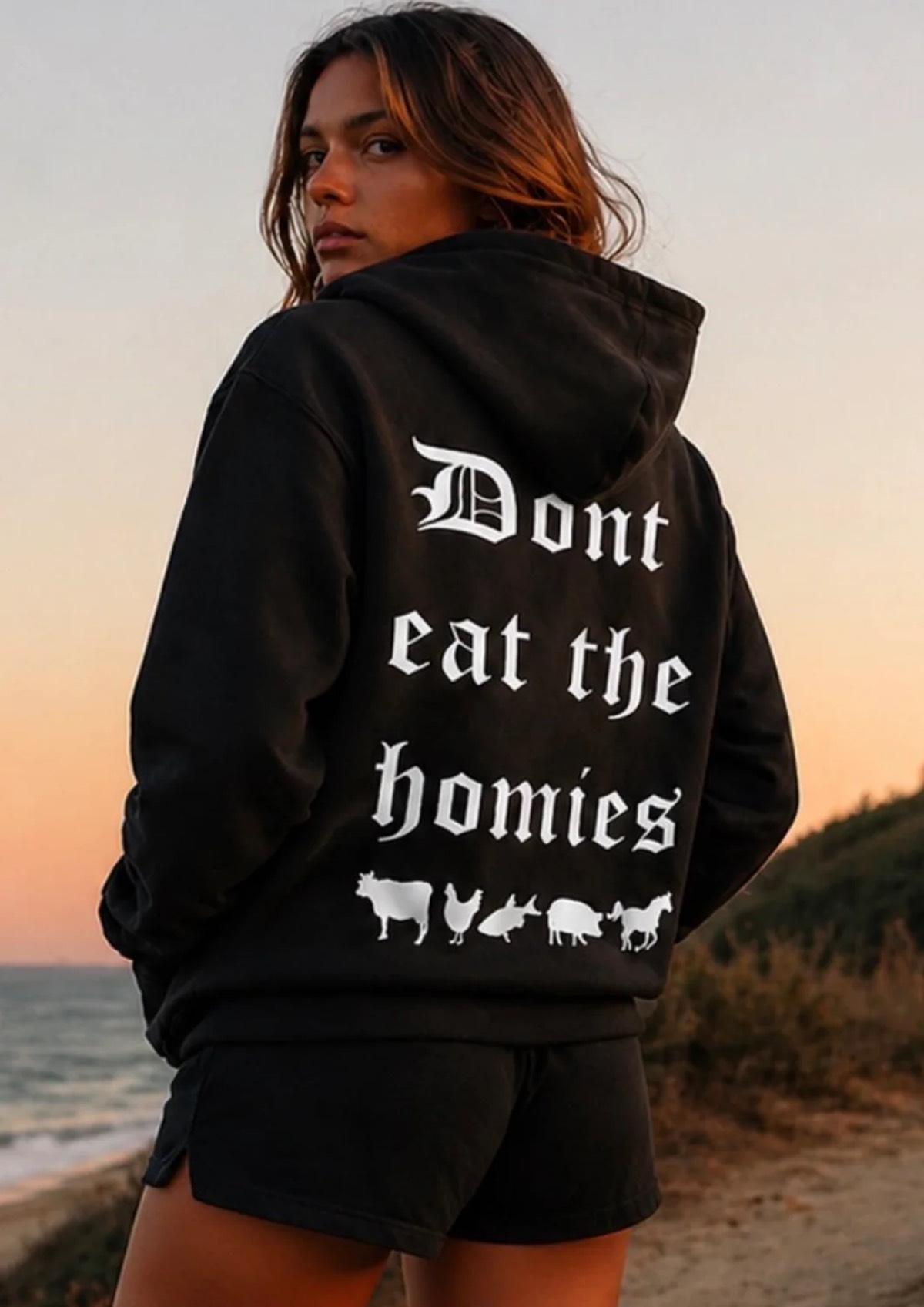 Woman in the sunset looking over her shoulder showing the back of her "Don't Eat the Homies" vegan hoodie.