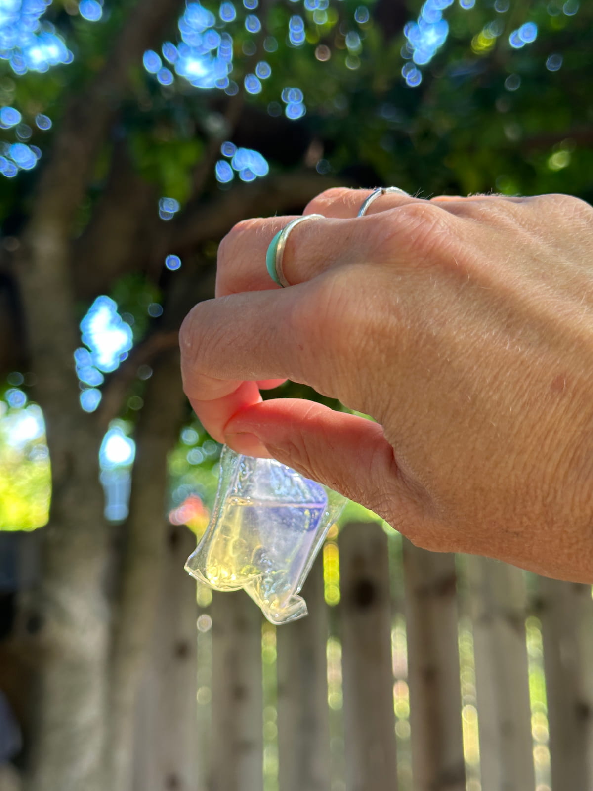 A hand holding up a clear plastic laundry pod from the company dropps.