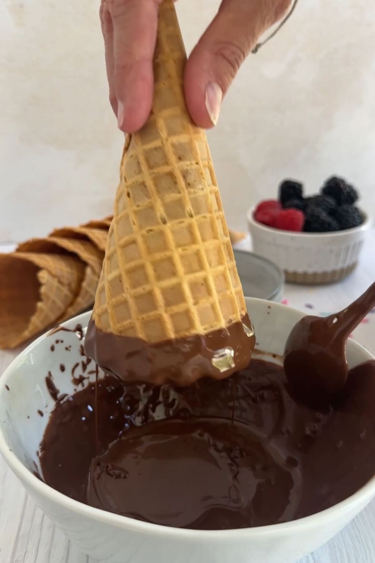 An ice cream cone held upside-down over a bowl of vegan melted chocolate.