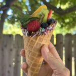 A hand holding up a fruit cone.