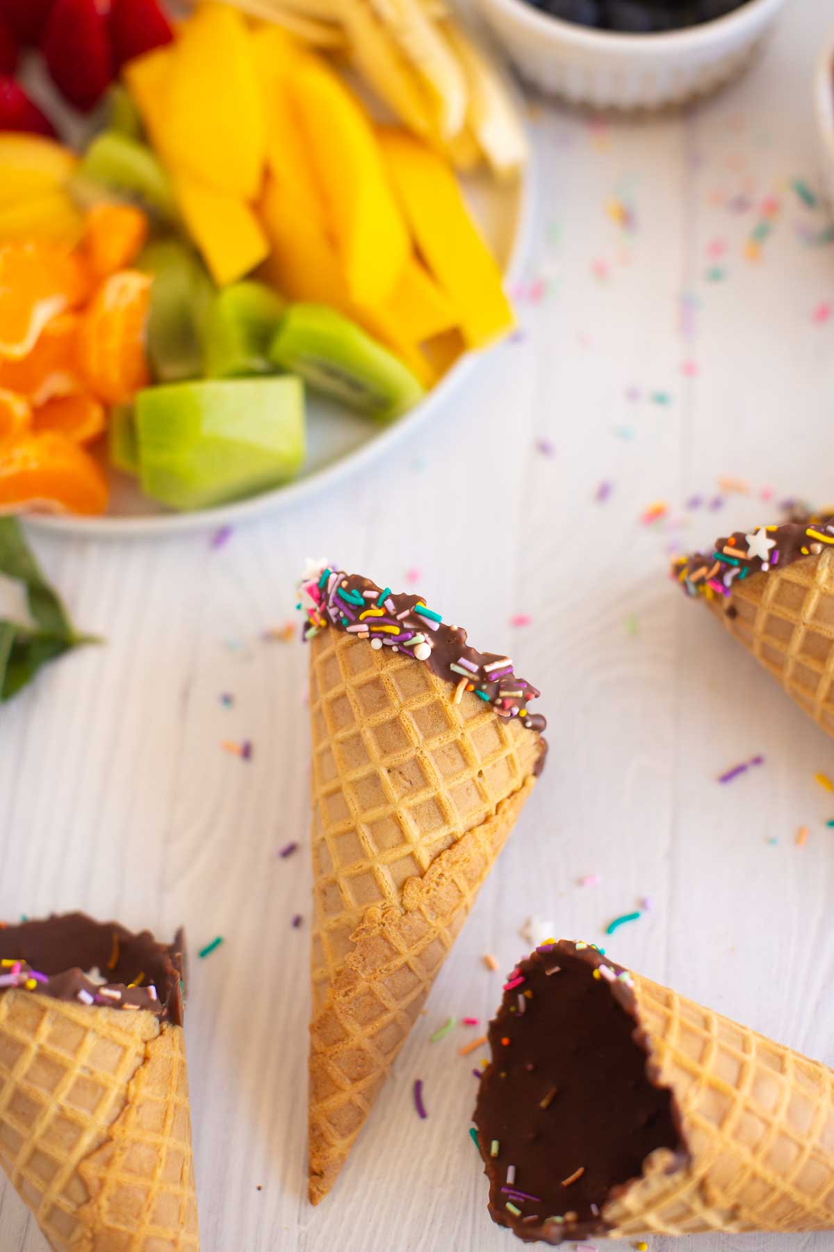 Chocolate-dipped ice cream cones with a bowl of fruit.