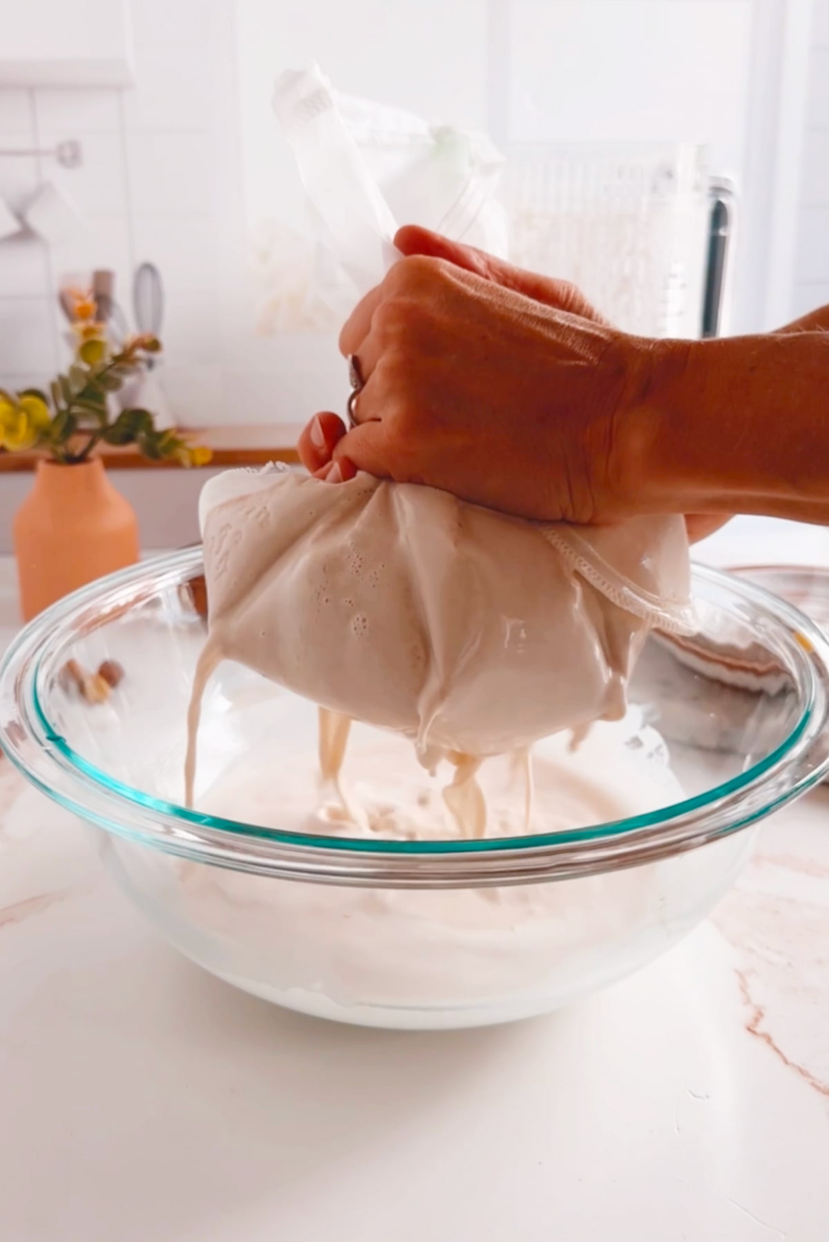 Straining vegan coffee creamer with a nut milk bag to remove the solids.