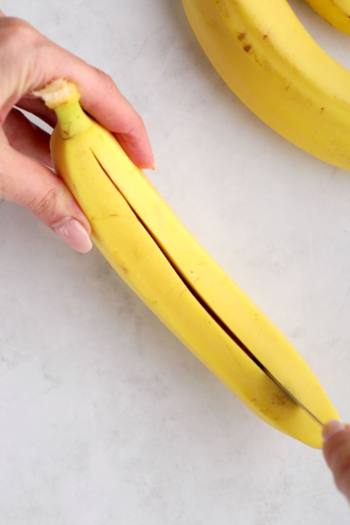 A banana with the peel on being sliced lengthwise.