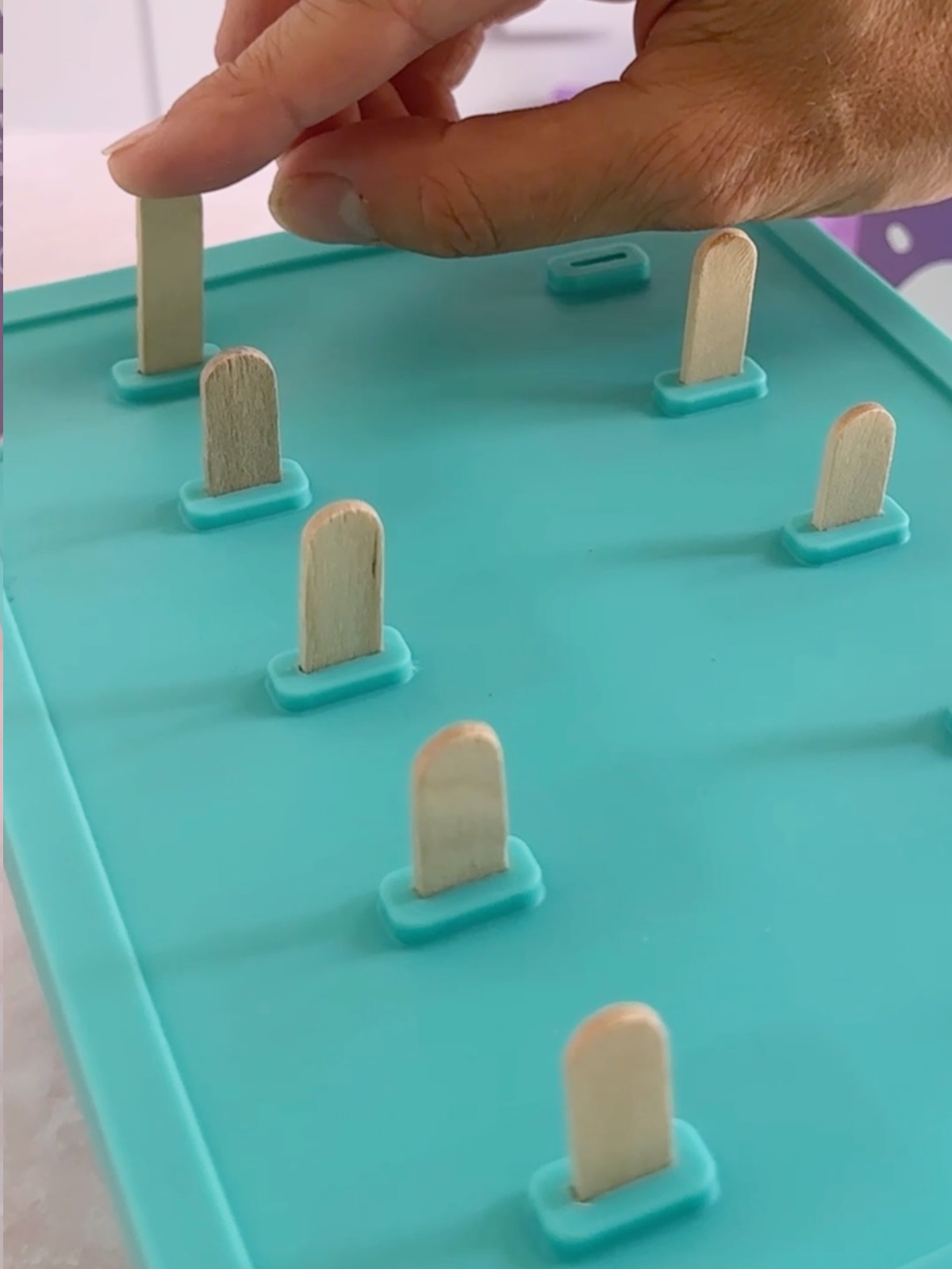 Pushing wooden popsicle sticks into the popsicle mold lid. 