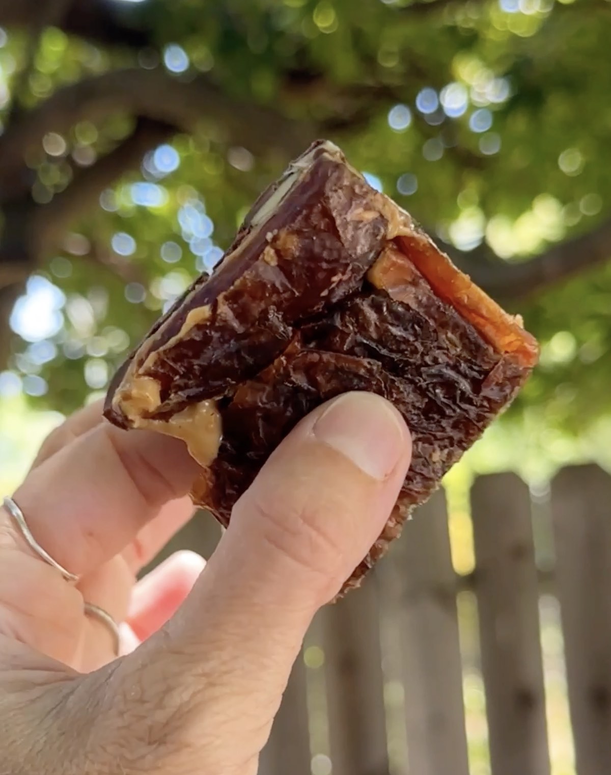 Holding out a square slice of homemade date bark, showing the bottom with medjool dates pressed together. 