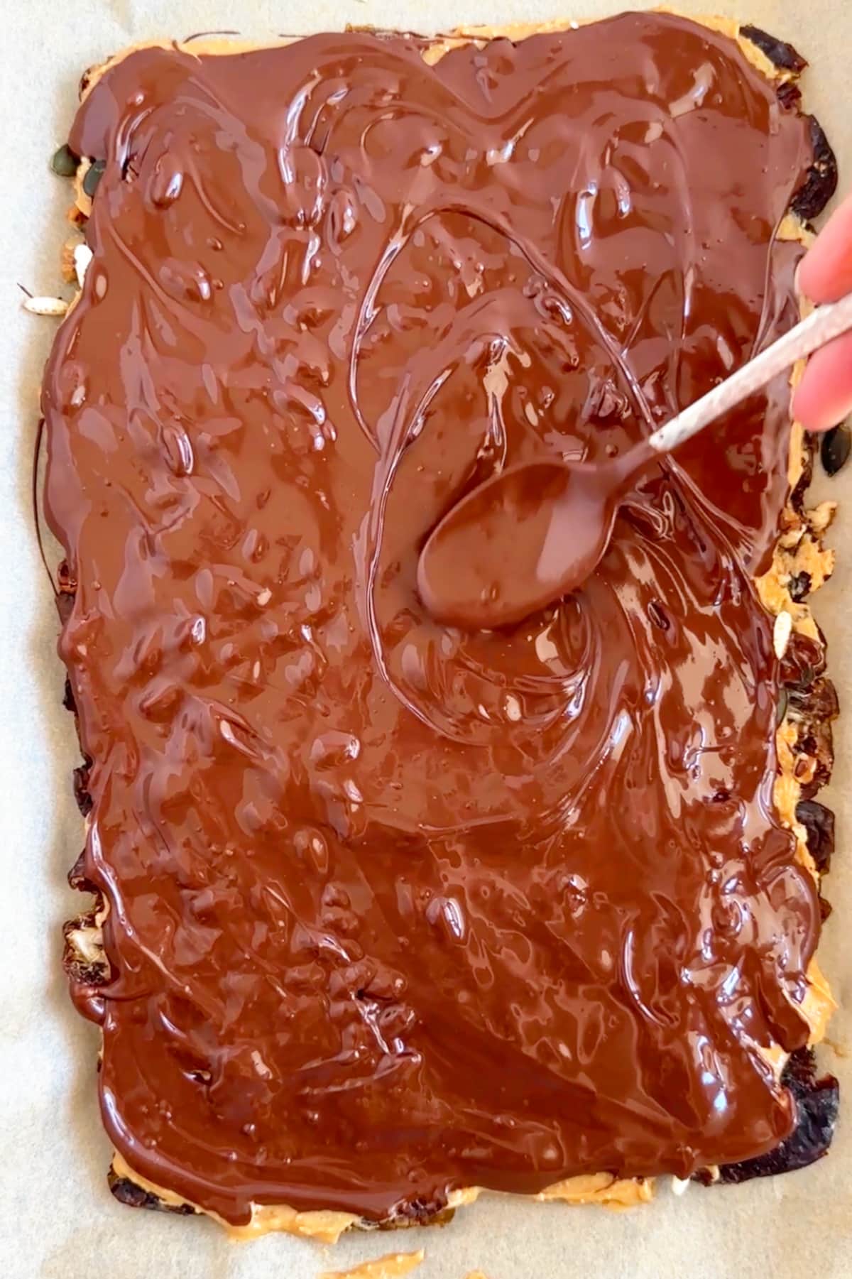 Melted chocolate being spread over the toppings with a spoon.