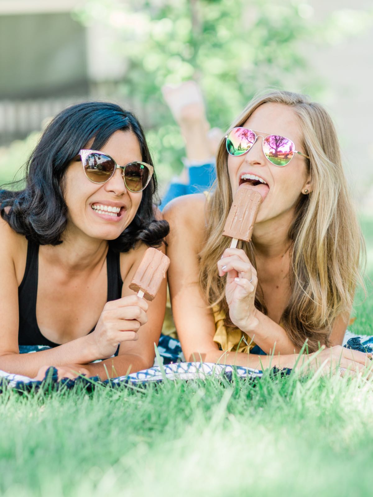 Toni Okamoto and Michelle Cehn lay on a picnic blanket, smiling and eating homemade fudgesicles.