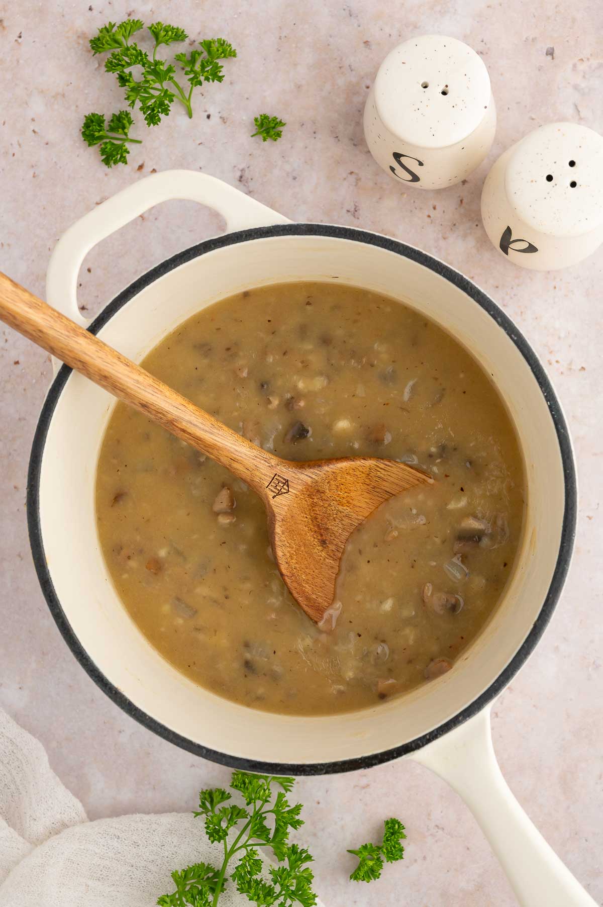 Vegan mushroom gravy in a pot with a wooden spoon with salt and pepper.
