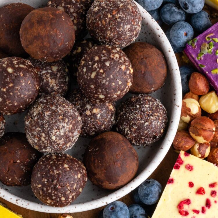 A plate stacked with vegan protein balls coated with chocolate cocoa powder and chopped hazelnuts.
