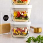 Meal prepped couscous bowls in sealable containers stacked on one another.
