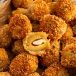 Fried olives in a basket with one sliced in half displaying the stuffed olive instead of the fried breading.