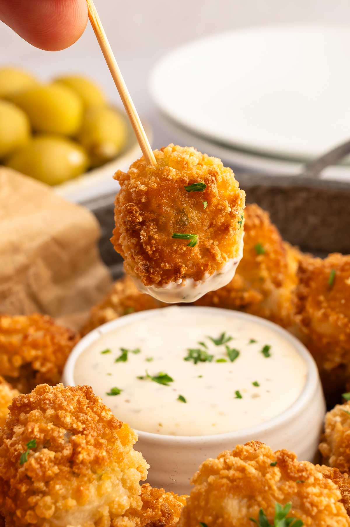 A fried olive dipping into a bowl of creamy sauce.