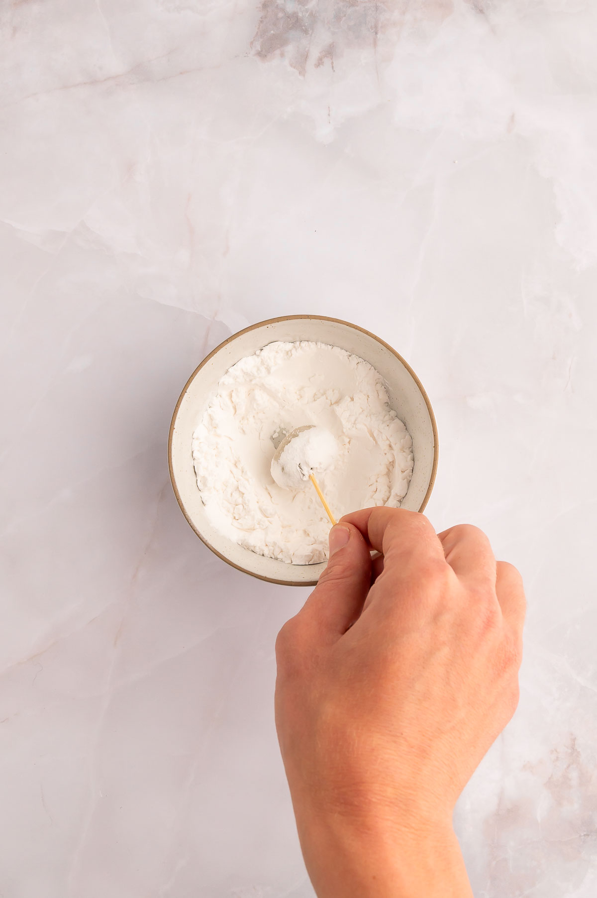 An olive on a toothpick dipped into a bowl of cornstarch.