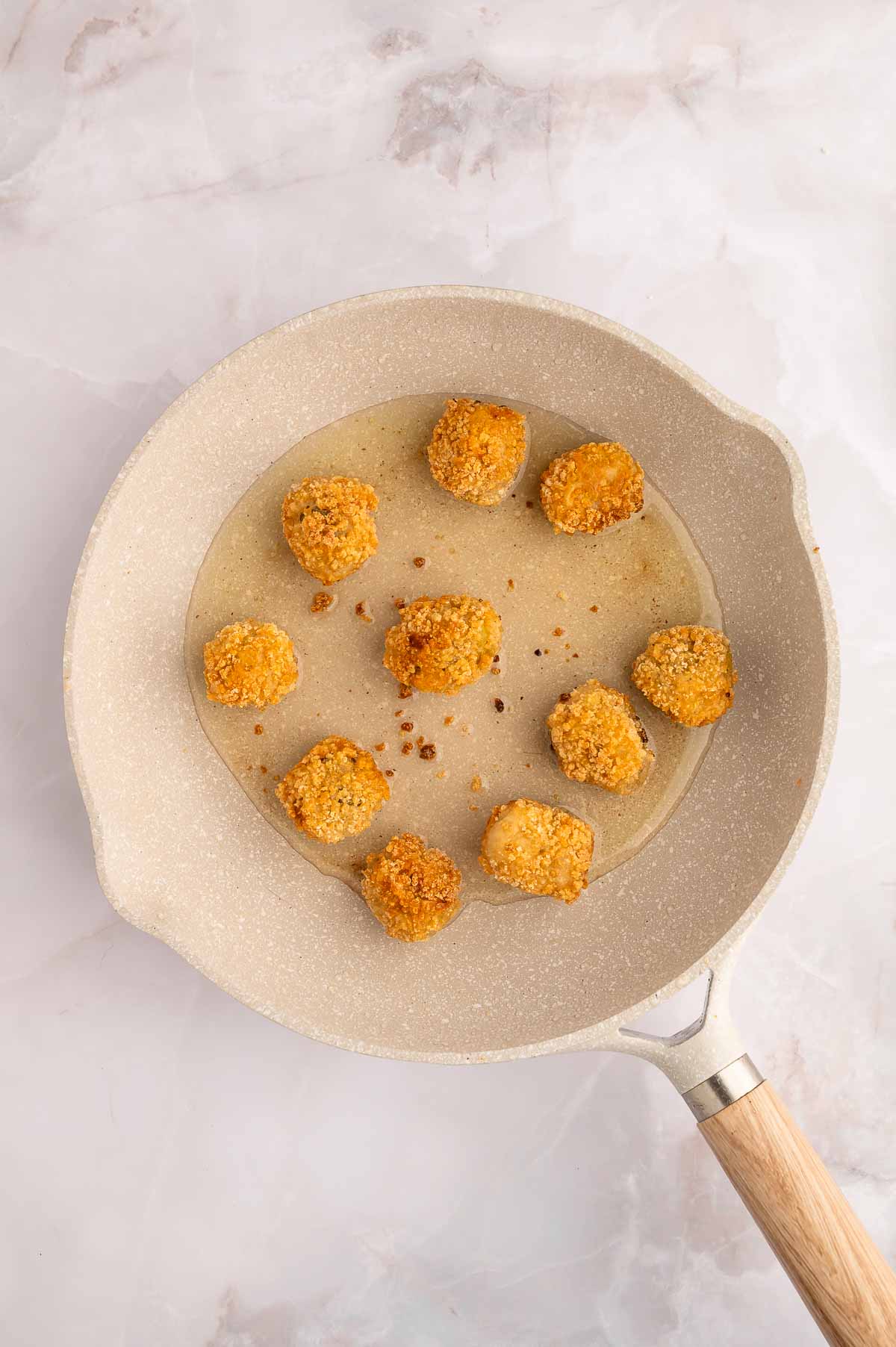 Stuffed olives frying in a skillet with oil.