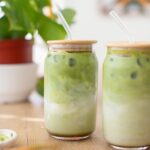 Two glasses of iced matcha lattes with glass straws.