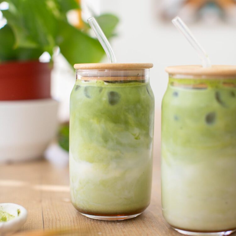 Two glasses of iced matcha lattes with glass straws.