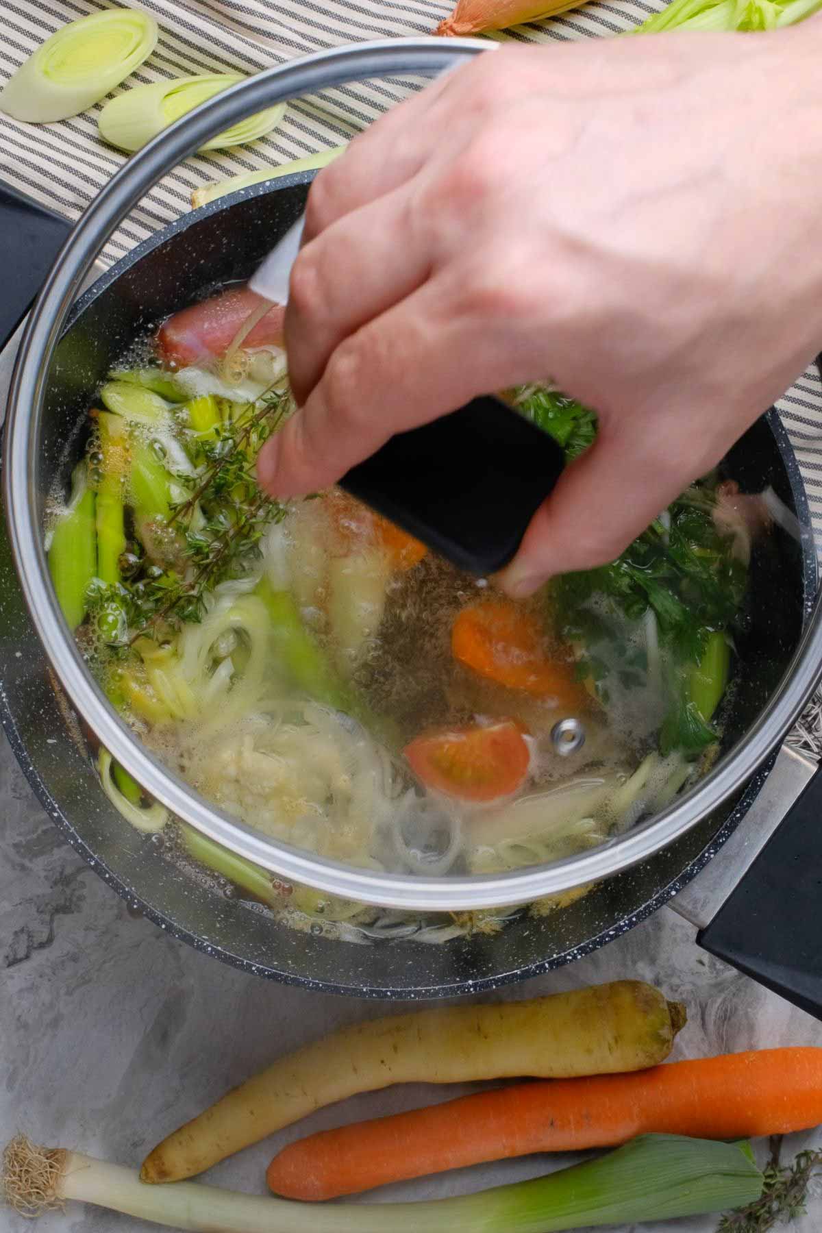 A lid being placed on a pot of vegetable scraps.