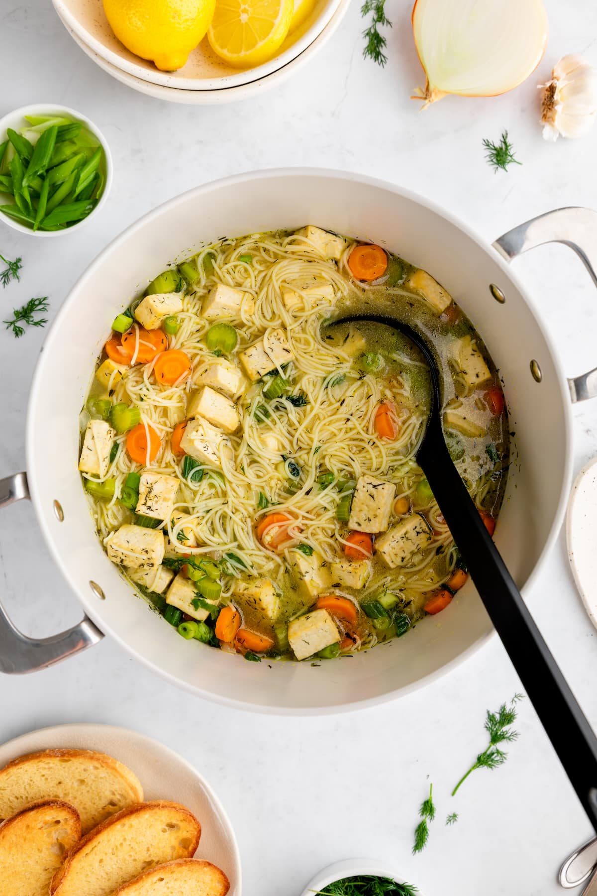 A pot of vegan chicken noodle soup with a large serving spoon.
