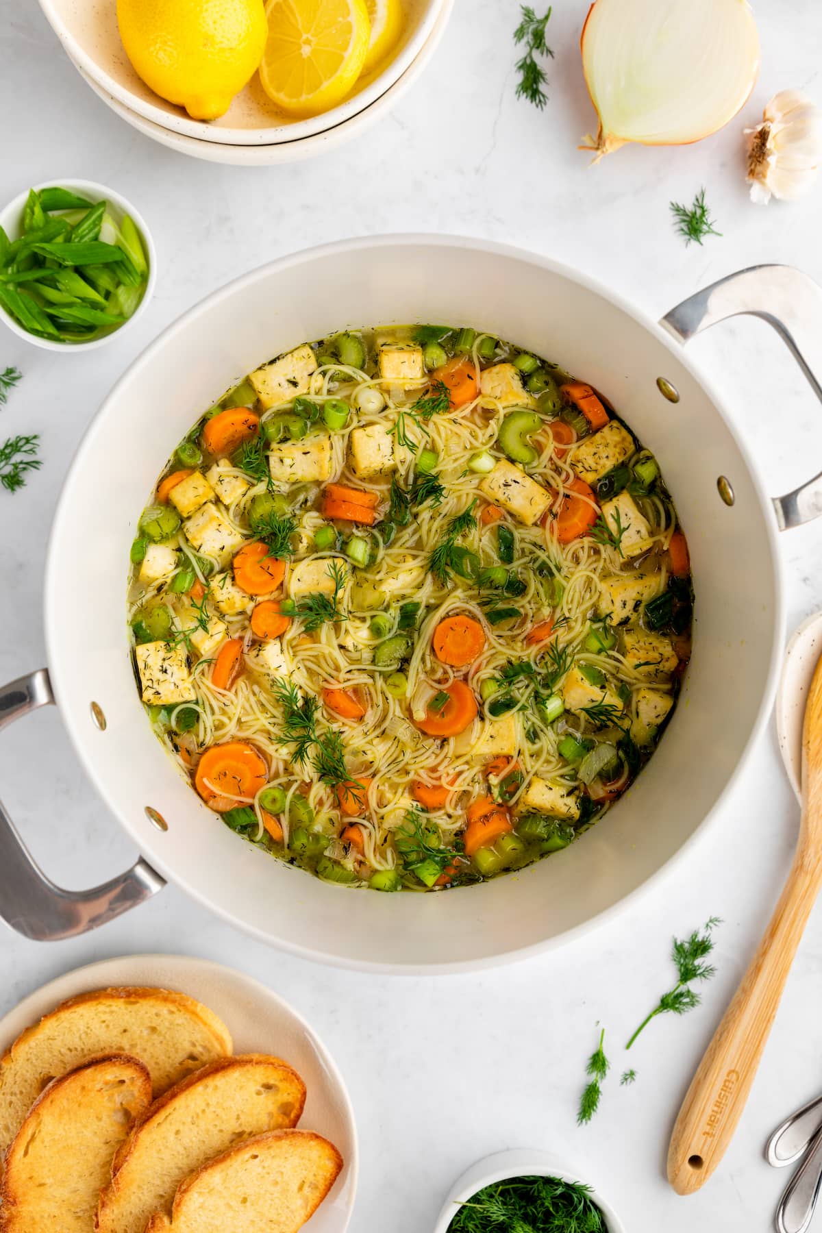 A large soup pot of vegan chicken noodle soup, sprinkled with fresh dill on top.