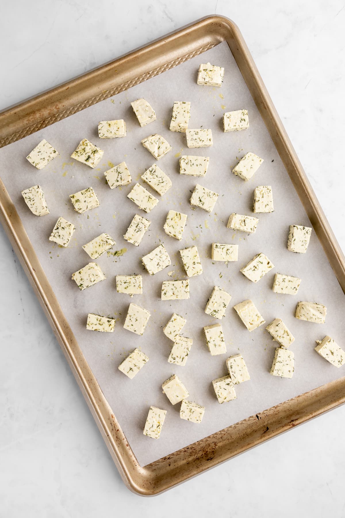 Herbed cubed tofu spread out on a baking tray lined with parchment paper.