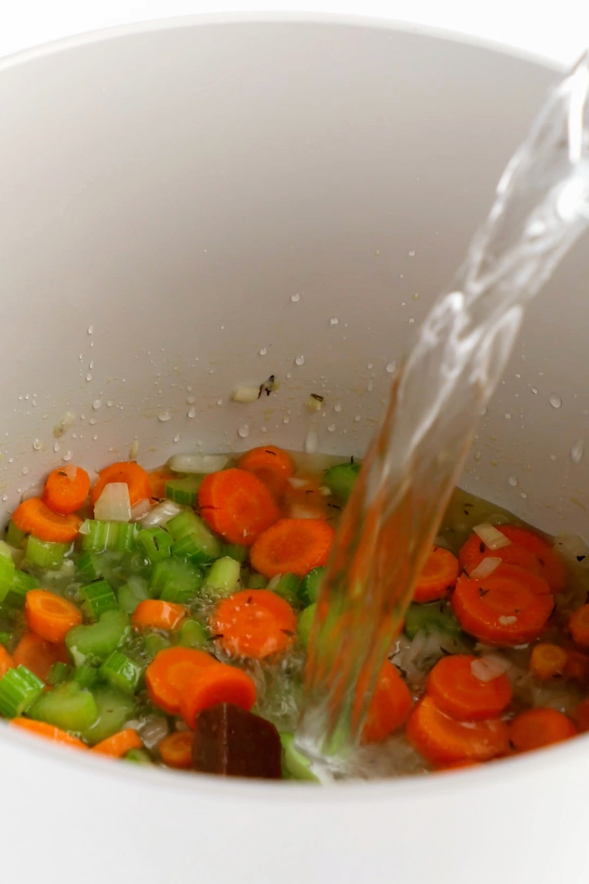 Water and vegetable bouillon being added to the pot of cooked vegetables for the soup.