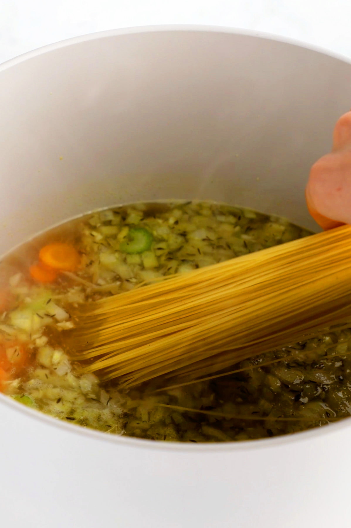 A pot of vegan chicken noodle soup with angel hair spaghetti added to the pot.