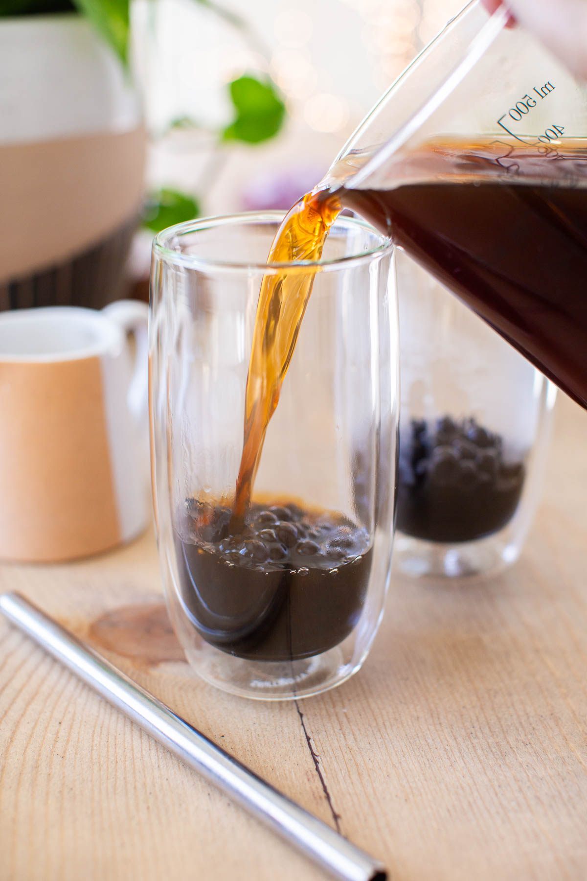 Coffee being poured into a glass over cooked tapioca pearls.