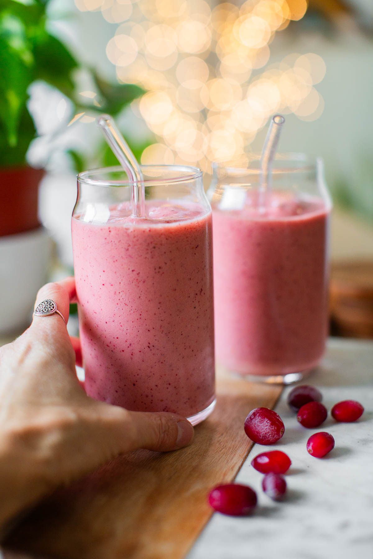 A hand reaching for a glass of pink cranberry smoothie.