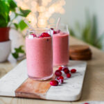 Two glasses of cranberry smoothie on a cutting board, topped with frozen cranberries.