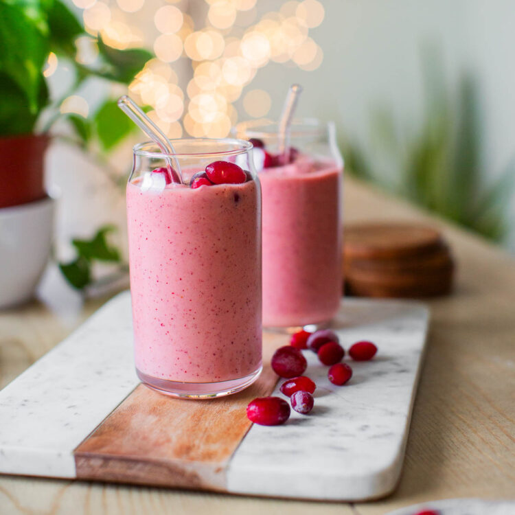 Two glasses of cranberry smoothie on a cutting board, topped with frozen cranberries.