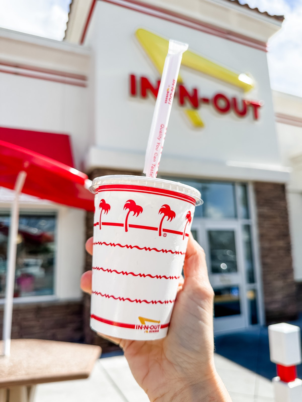 A vegan woman holding out a cup for iced tea in front of In N Out Burger in California.