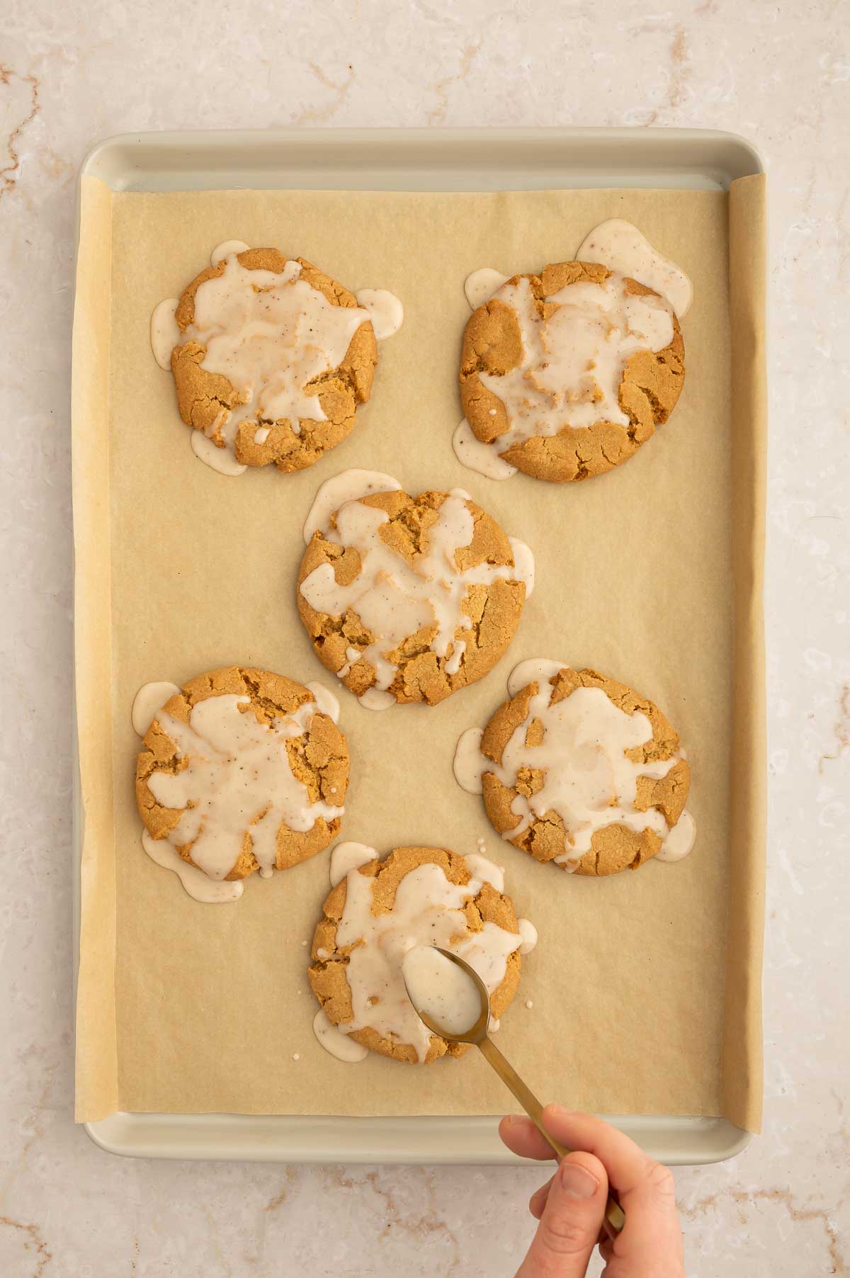 Vegan chai cookies being iced on a baking sheet.
