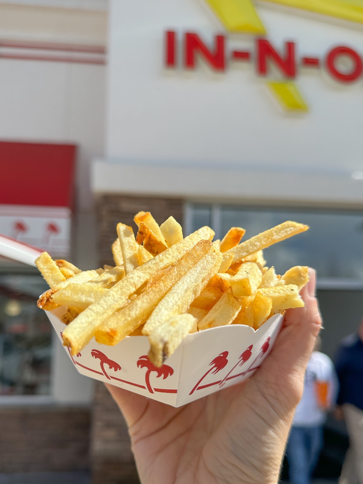 A container of vegan fries at In N Out held out in front of the restaurant sign. 