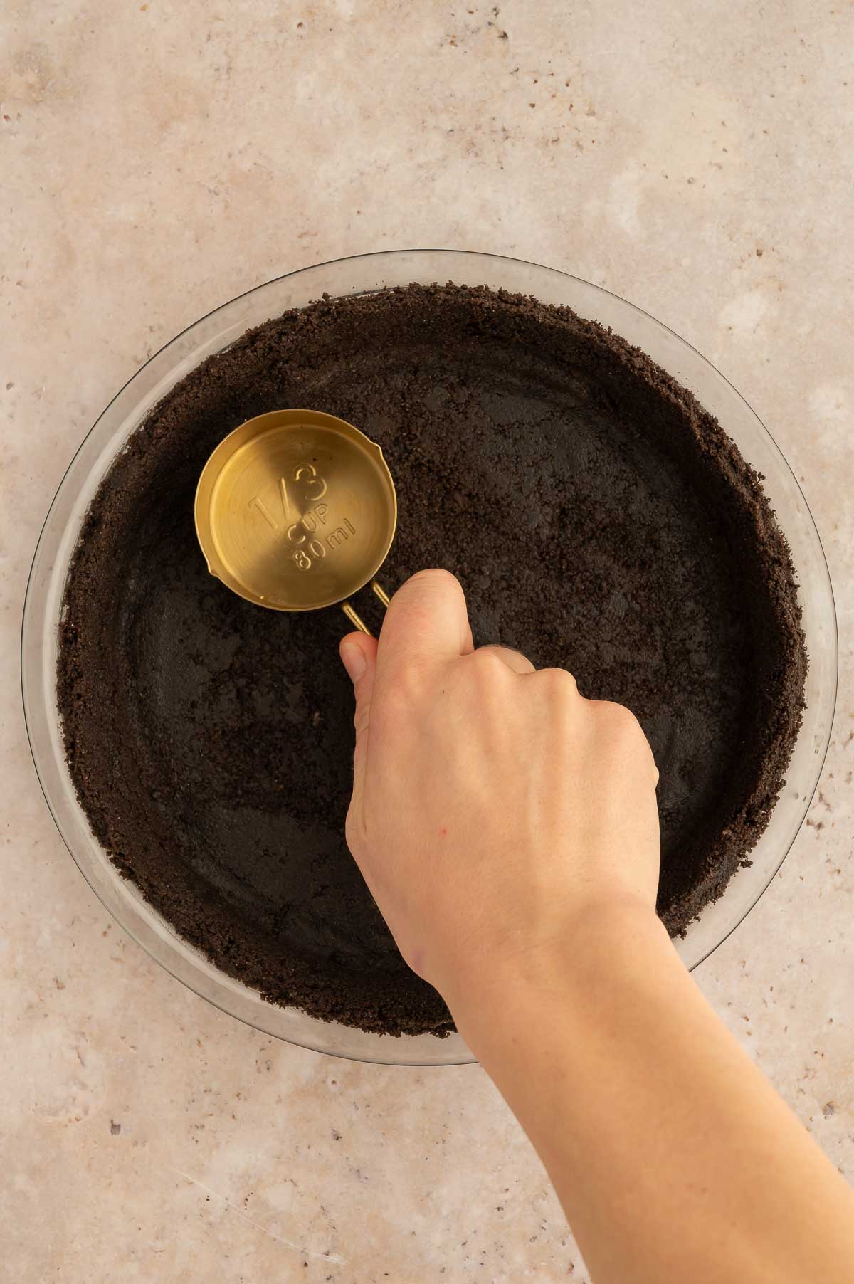 A oreo cookie crust being pressed into a pie dish.