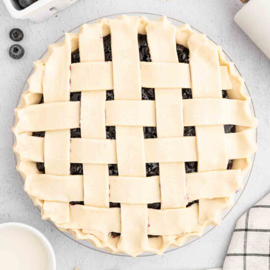 Prepared vegan pie crust with a lattice design, filled with blueberry pie filling.