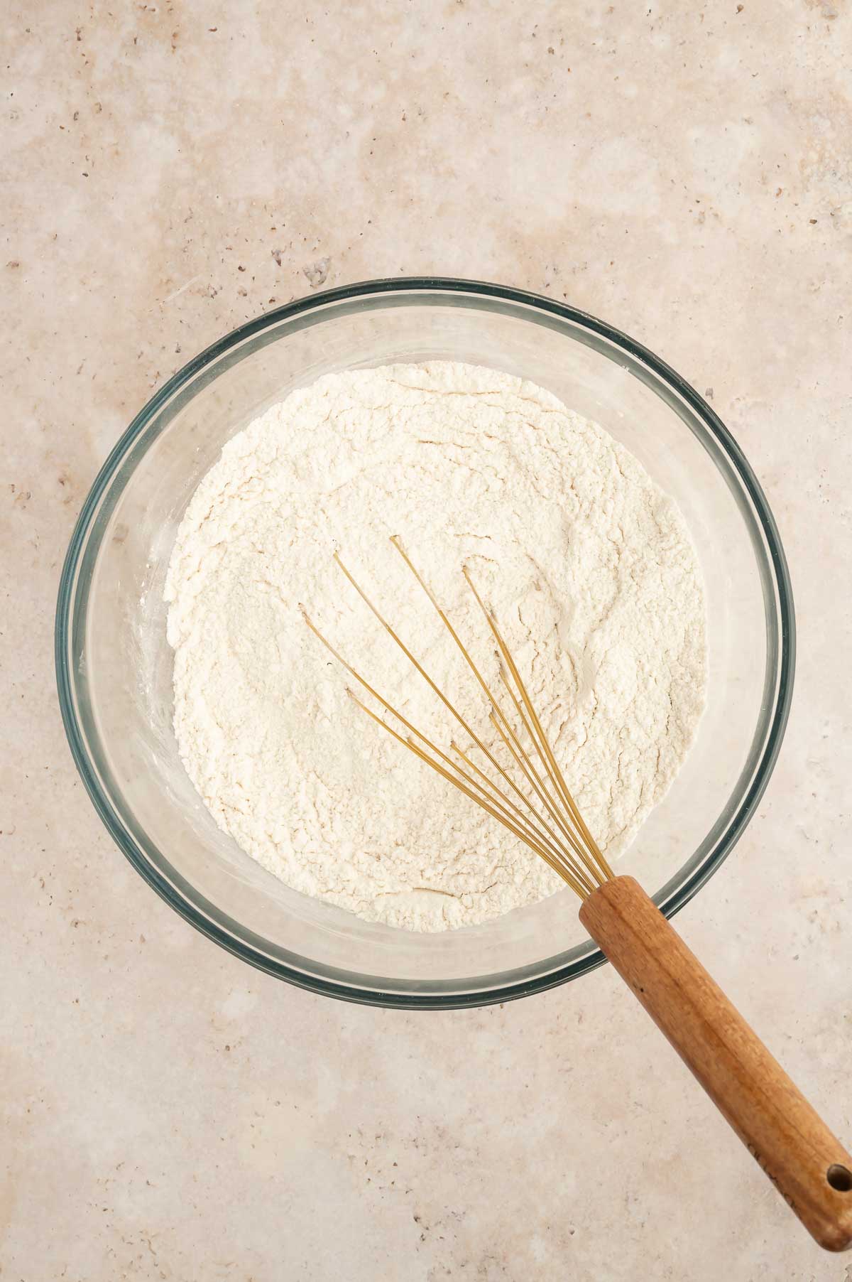 Dry ingredients for sponge cake sifted into a glass bowl with a wooden whisk.
