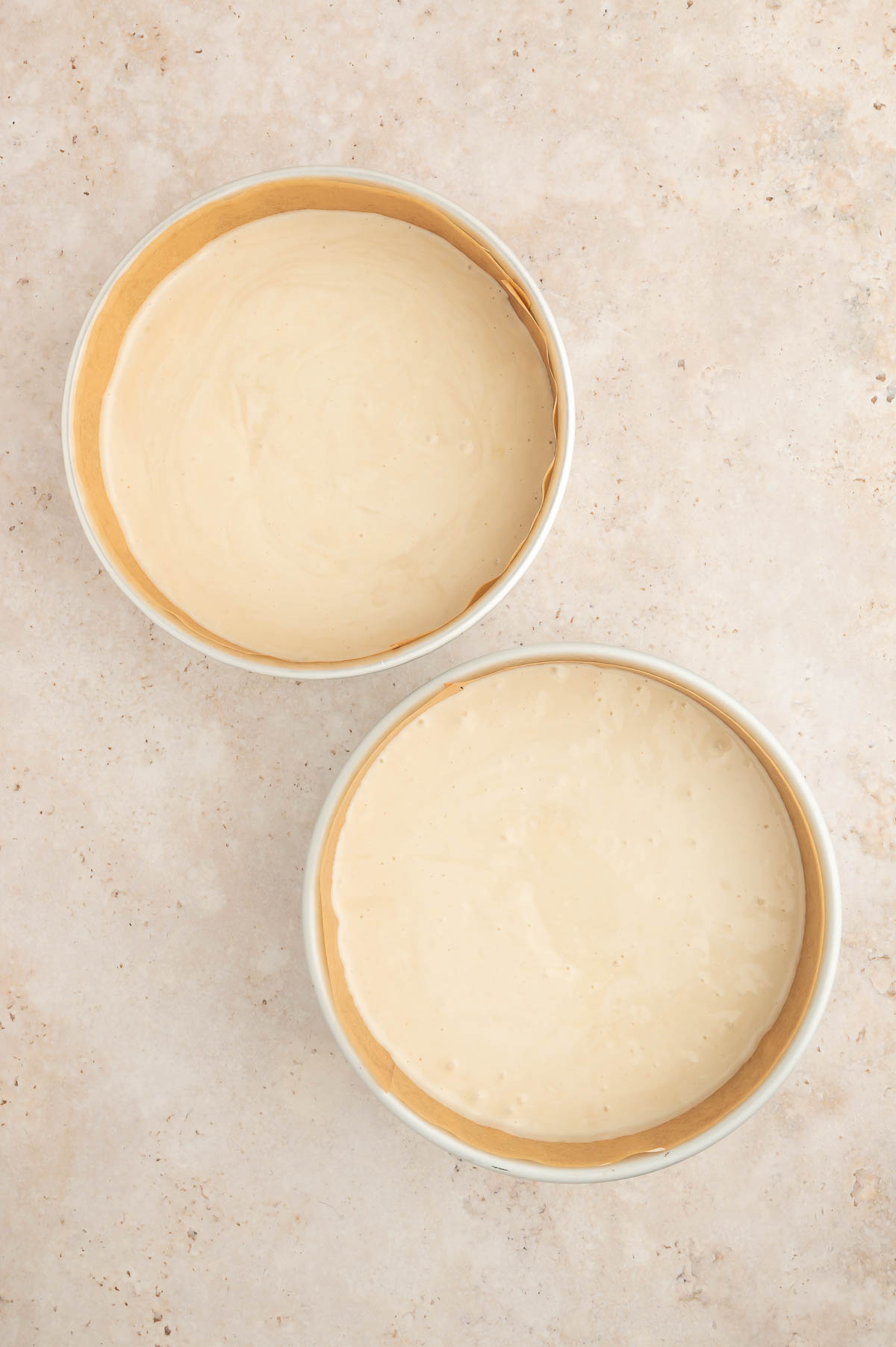 Evenly divided vegan sponge cake batter in two parchment-lined cake pans, ready to bake.